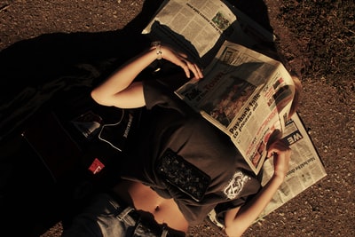 女人黑色t恤和黑色短裤坐在地上阅读报纸
